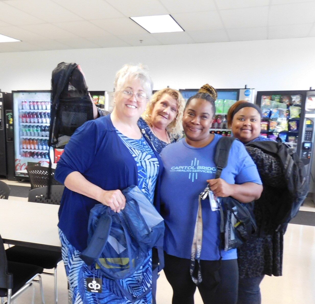 Four women smiling and holding backpacks