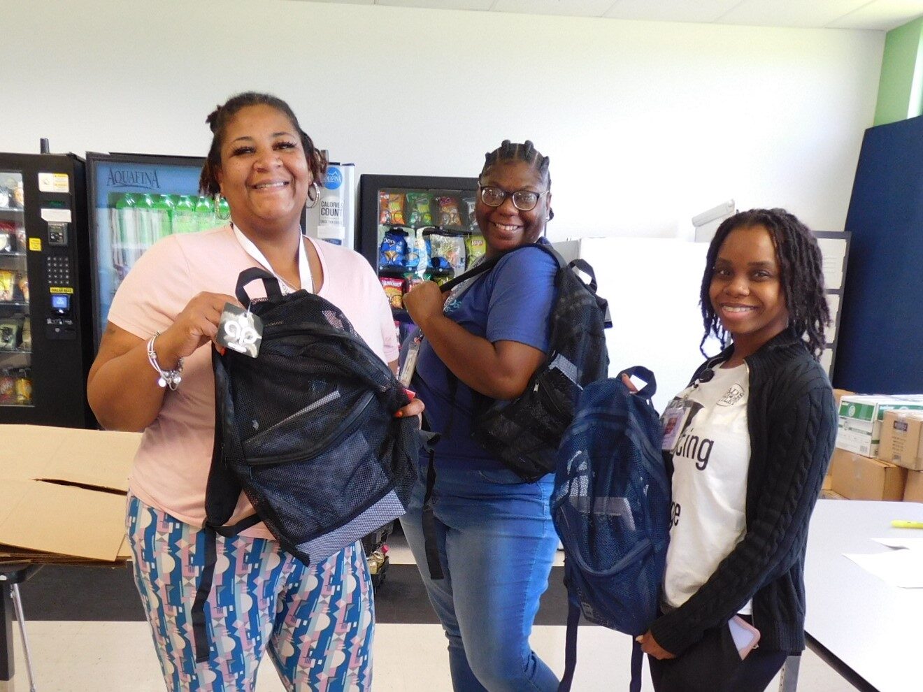 Three women smiling and holding backpacks